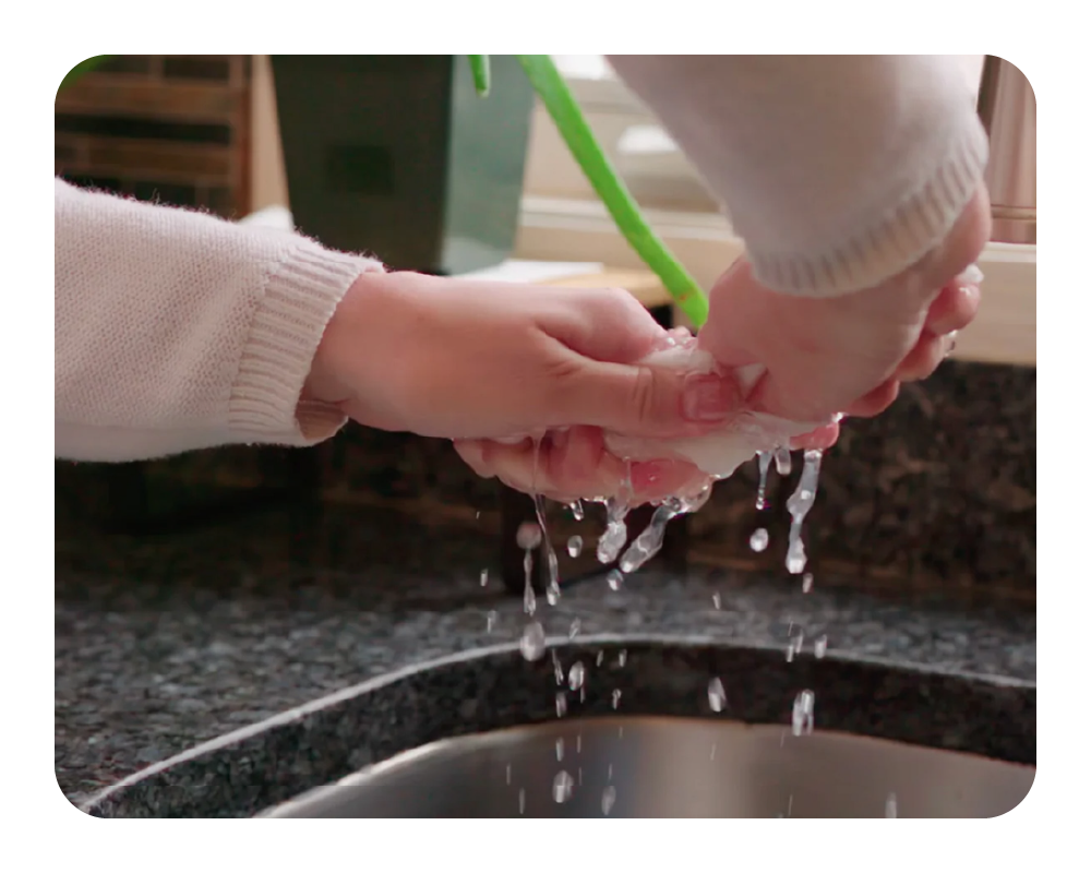Two hands under running water from a green faucet, with a blurred background.