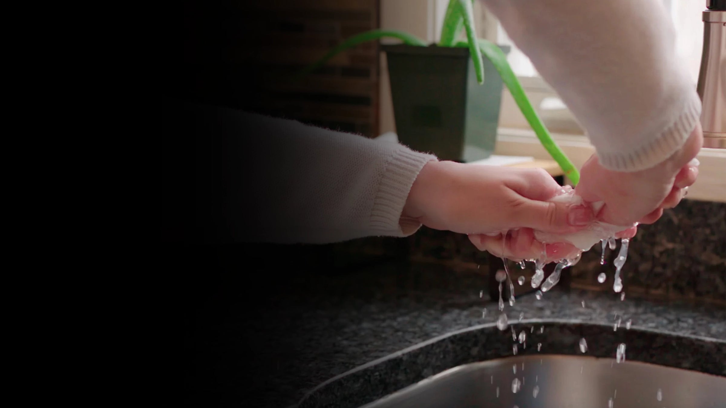 Person washing hands under running water in a kitchen sink.