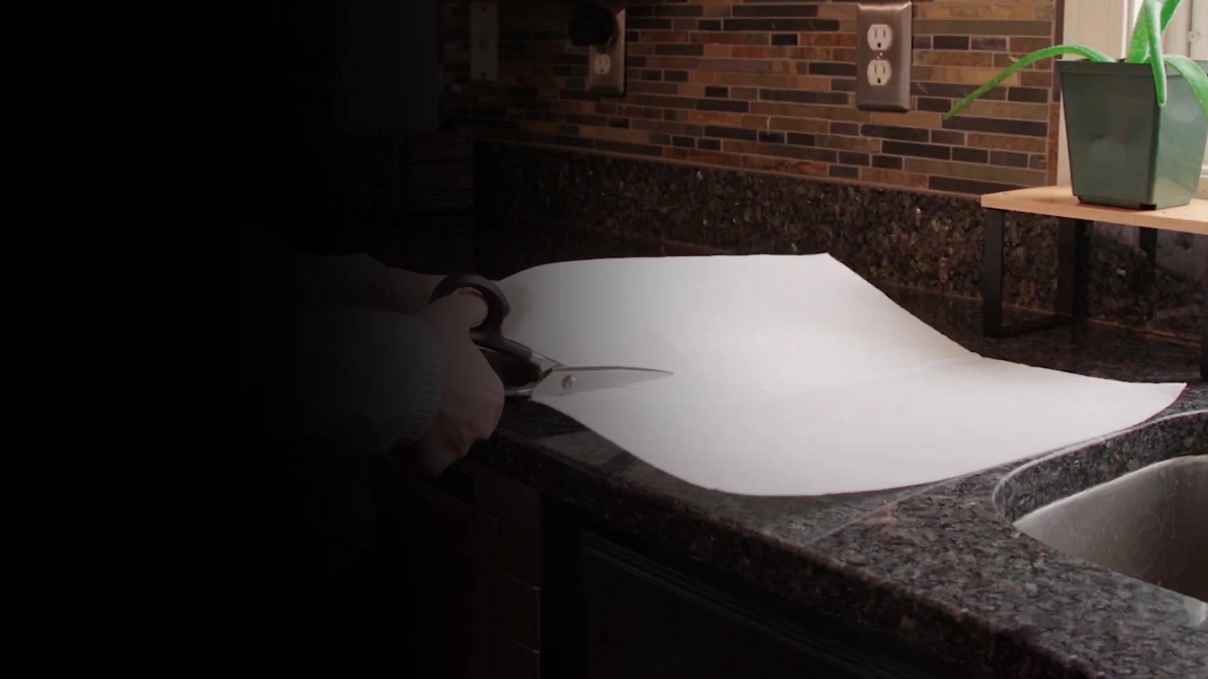 Person cutting a white mighty mat on a kitchen counter with scissors.