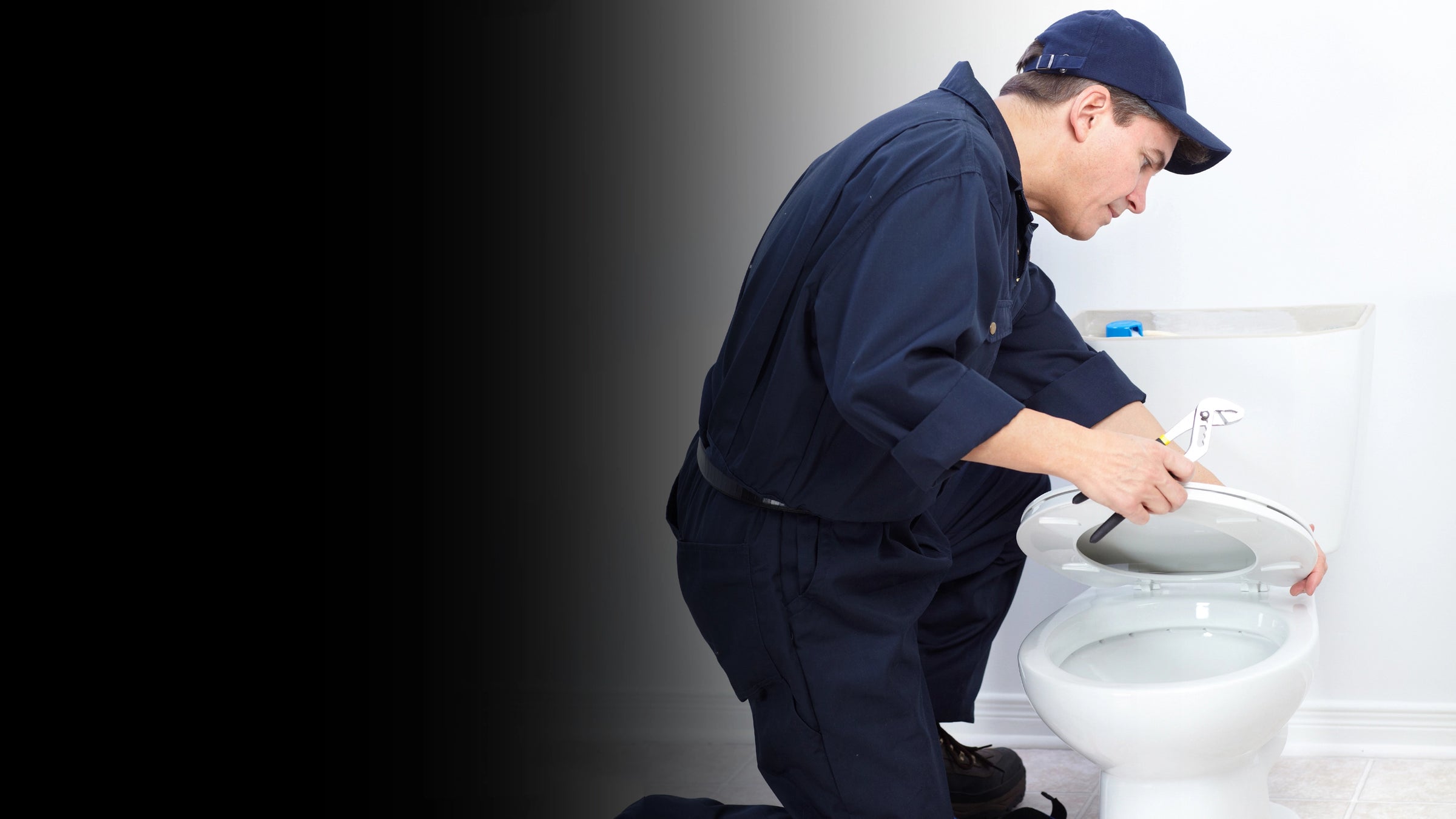 Plumber in blue uniform and cap fixing a toilet.