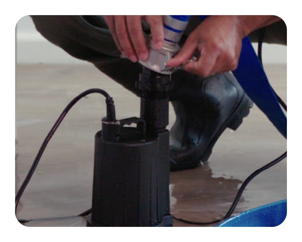 Person using a black submersible pump on a concrete floor.