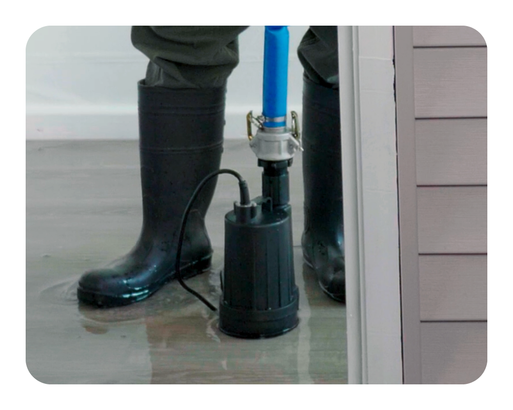 Person using a submersible pump to remove water from a room with rubber boots on.