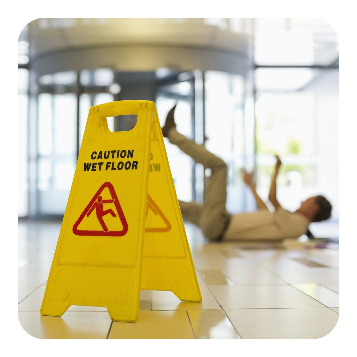 Yellow caution wet floor sign with a blurred background of a person falling on a wet floor.
