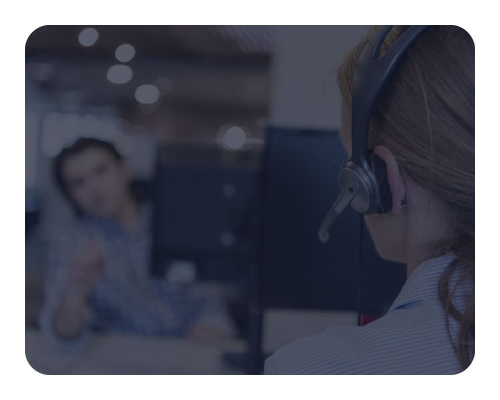 Person wearing a headset in an office setting with another person in the background.