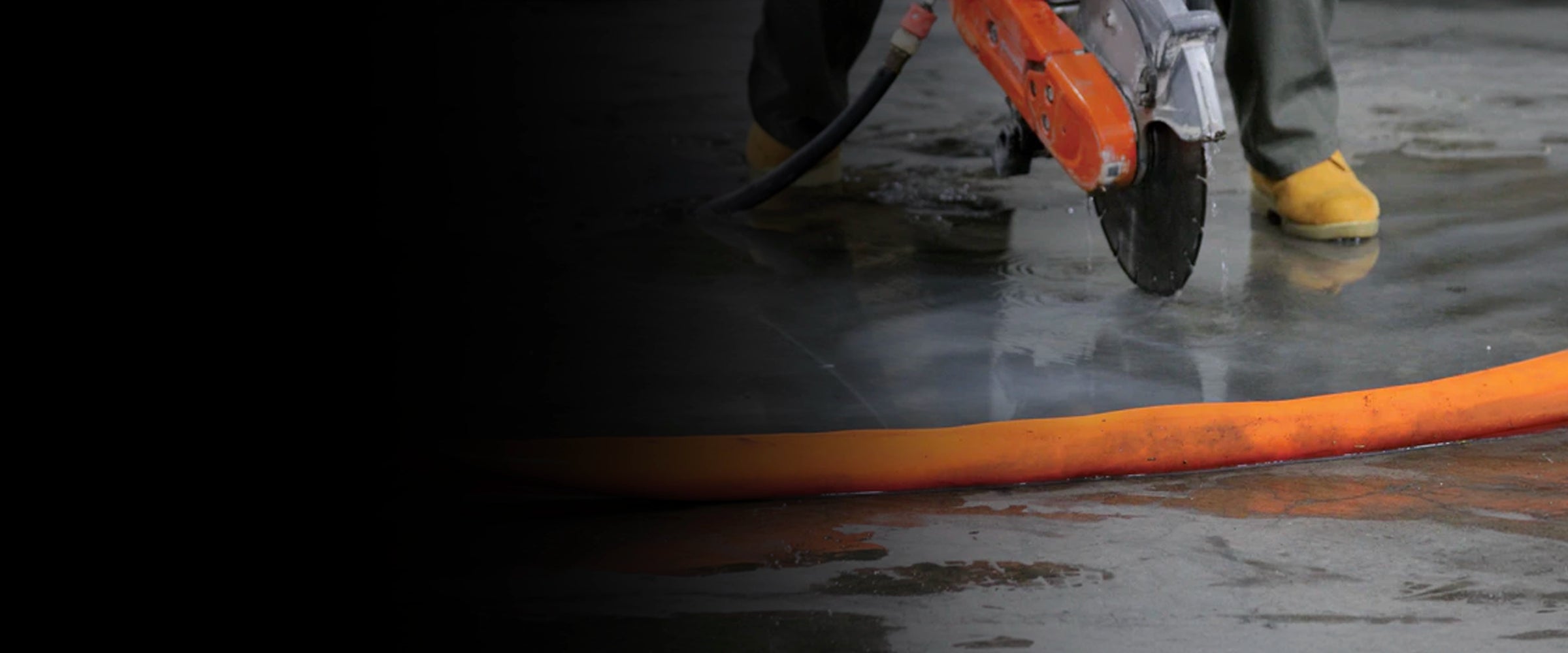 Person using a wet saw cutting tool with an orange water dam on a concrete surface