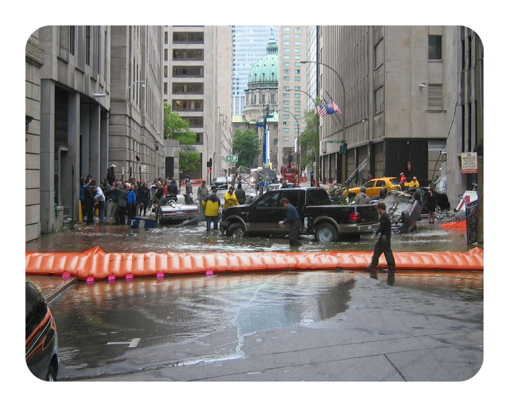 City street with flooded area and people around, surrounded by tall buildings with orange water force containing flood water
