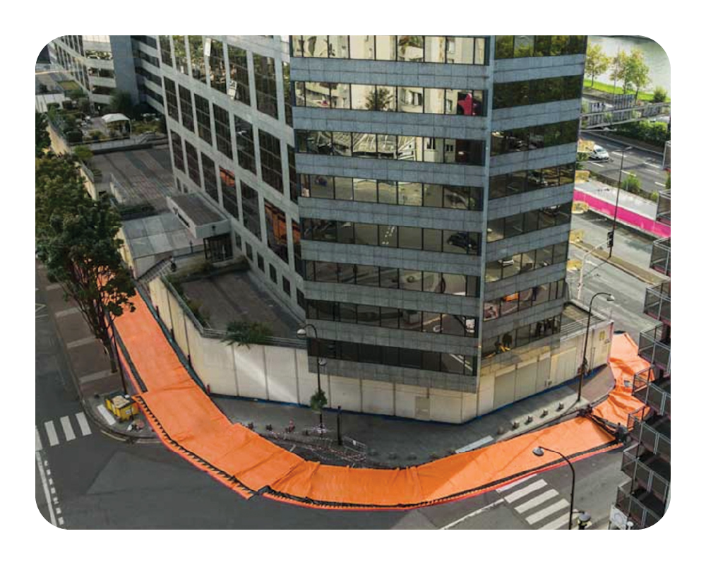Aerial view of a modern building with an orange water force barrier on a city street.