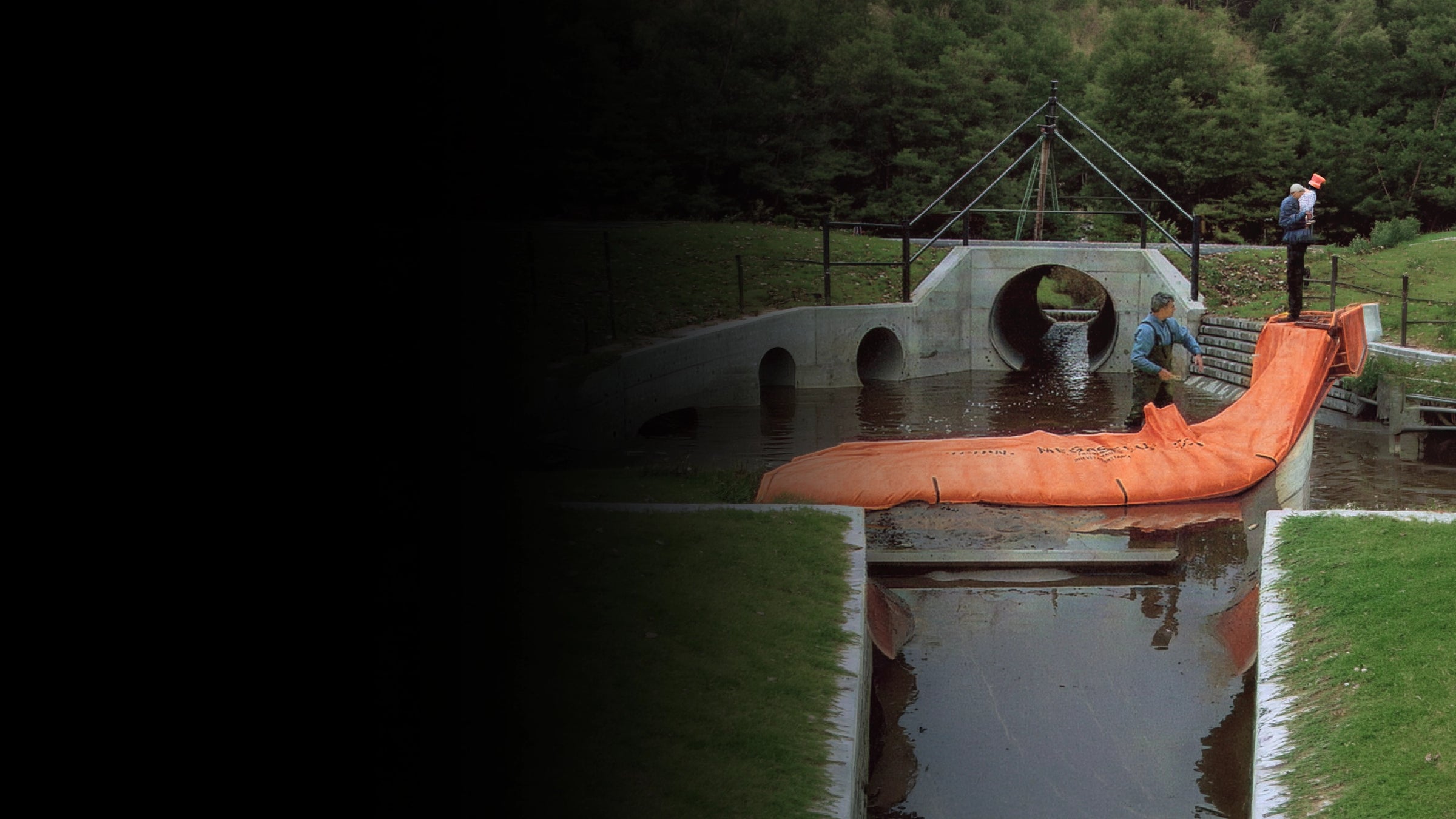Person using orange water force near a small bridge over water with trees in the background.
