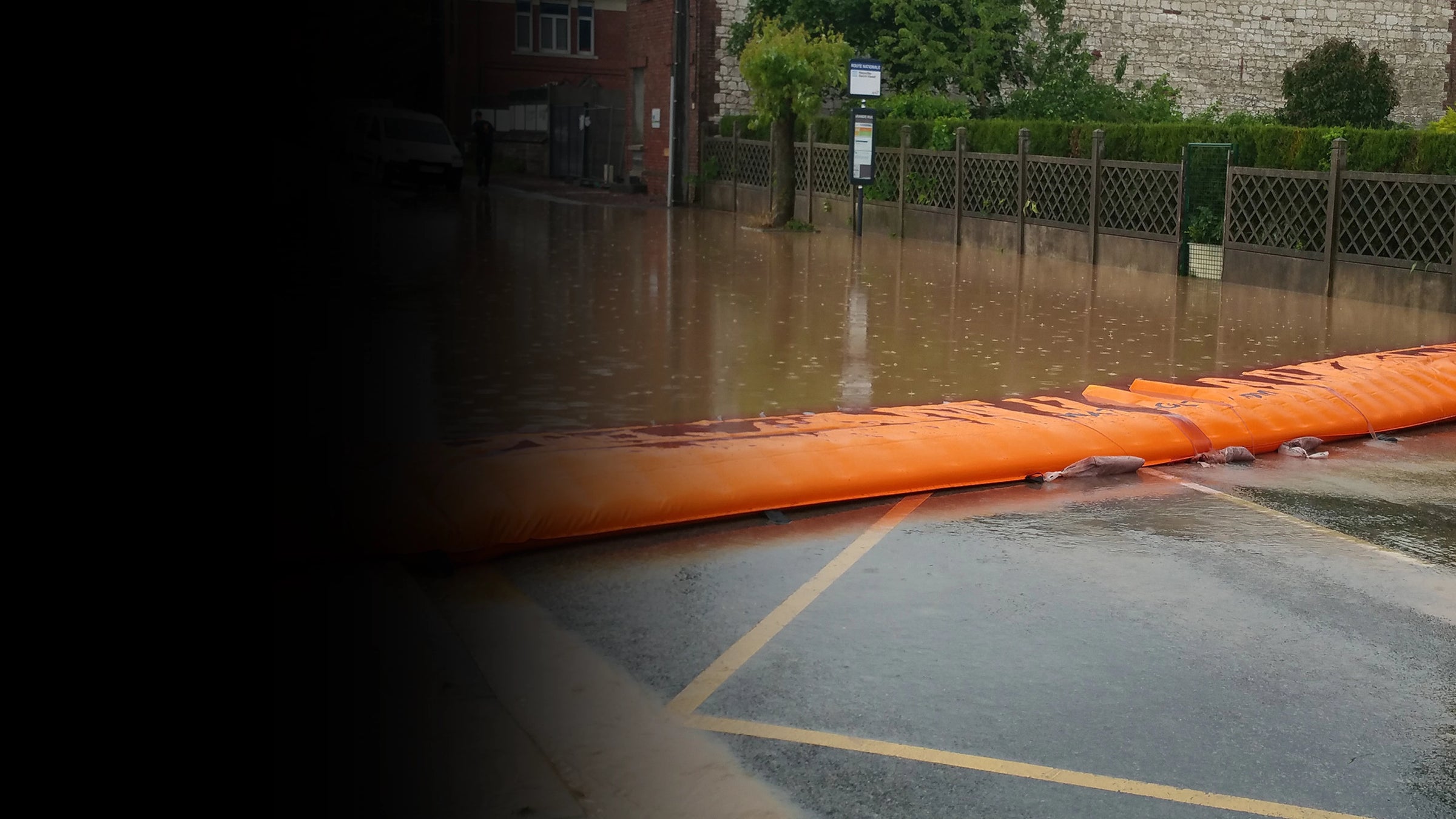 Flooded parking lot with orange water force and building in the background